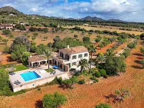 Una villa con piscina, rodeada por un jardín ajardinado y un paisaje montañoso.
