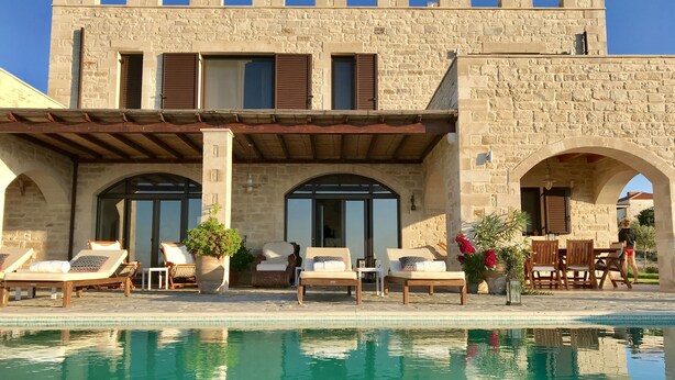 Ein Steinhaus mit Pool, Sitzgelegenheiten im Freien und bogenförmigen Durchgängen.