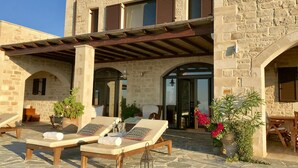 Ein Steinhaus mit überdachter Terrasse, auf der Lounge-Stühle und Blumentöpfe stehen.