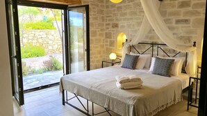 Ein Schlafzimmer mit Bett, Nachttisch, Lampe und Blick ins Freie durch eine Glastür.