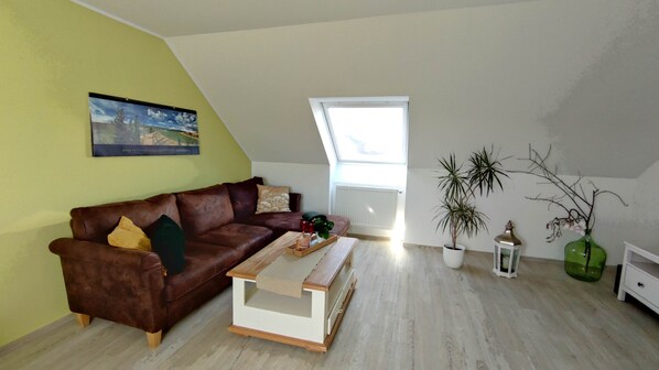 A living room with a brown leather sofa, a wooden coffee table, a potted plant, and a window with a view. - Very light, friendly apartment for 2 to 4 people with WiFi (Norden)