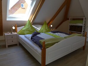 A bedroom with a sloped ceiling, a bed with green and blue bedding, a nightstand with a lamp, and a wooden wardrobe. - Very light, friendly apartment for 2 to 4 people with WiFi (Norden)