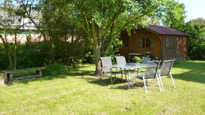 A wooden cabin with a dining table and chairs in a grassy area, surrounded by trees. - Very light, friendly apartment for 2 to 4 people with WiFi (Norden)