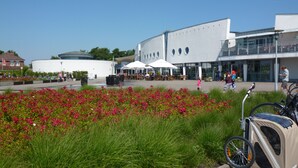 A modern building with a cafe and restaurant on the ground floor, surrounded by a garden with red flowers.
