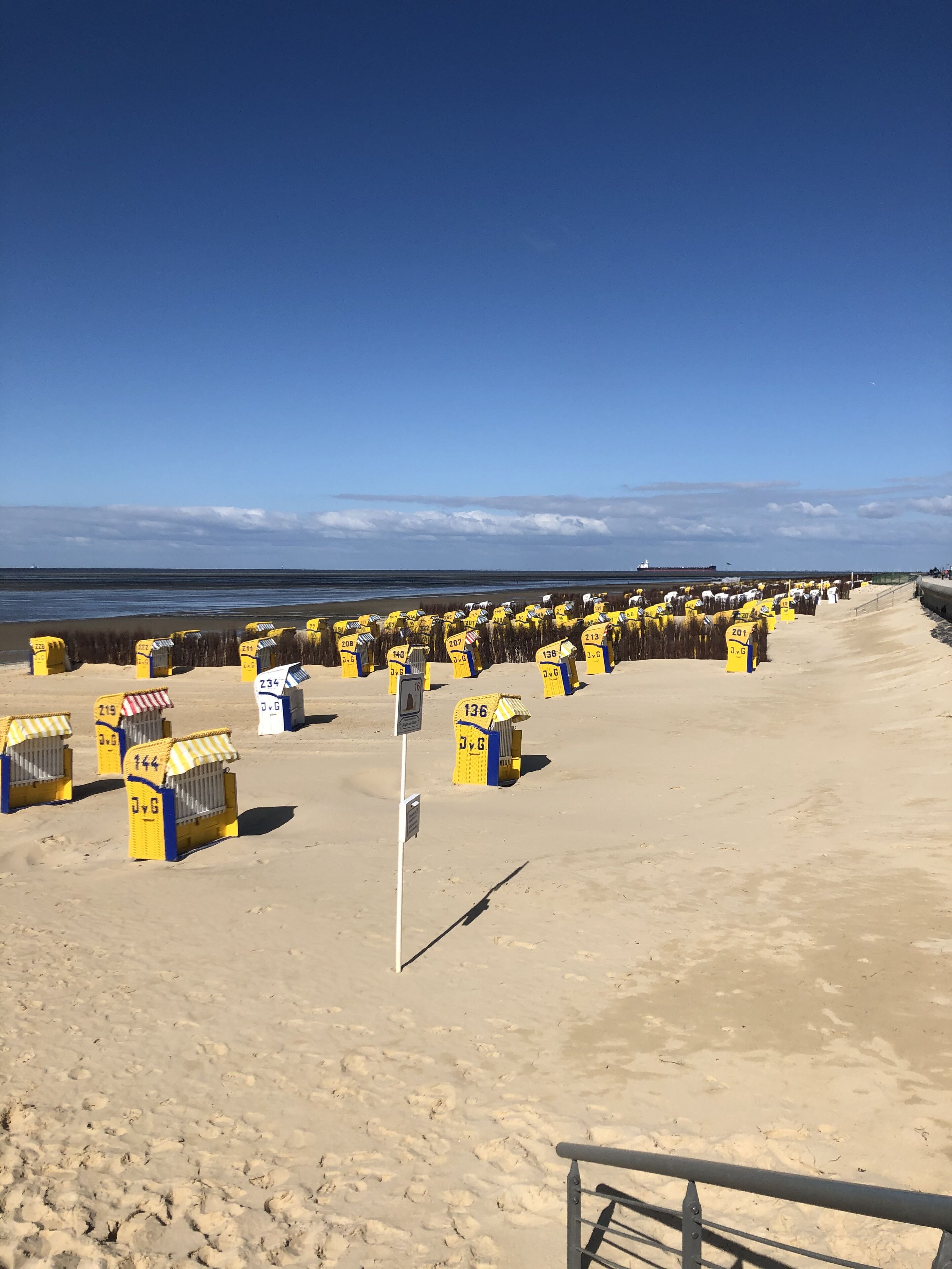 A beach with numerous yellow beach huts, each marked with a number and letters.