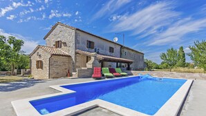Eine Steinvilla mit Swimmingpool und bunten Liegestühlen.