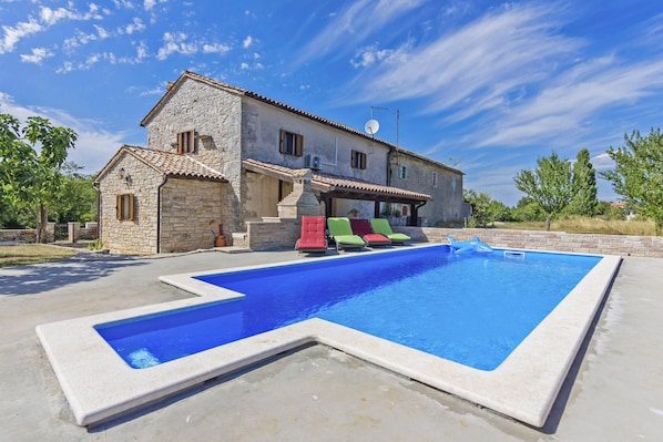 A stone villa with a swimming pool and colorful lounge chairs.