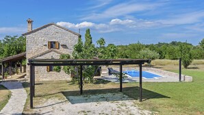 Ein Steinhaus mit Pool, einer Pergola und einem Garten.