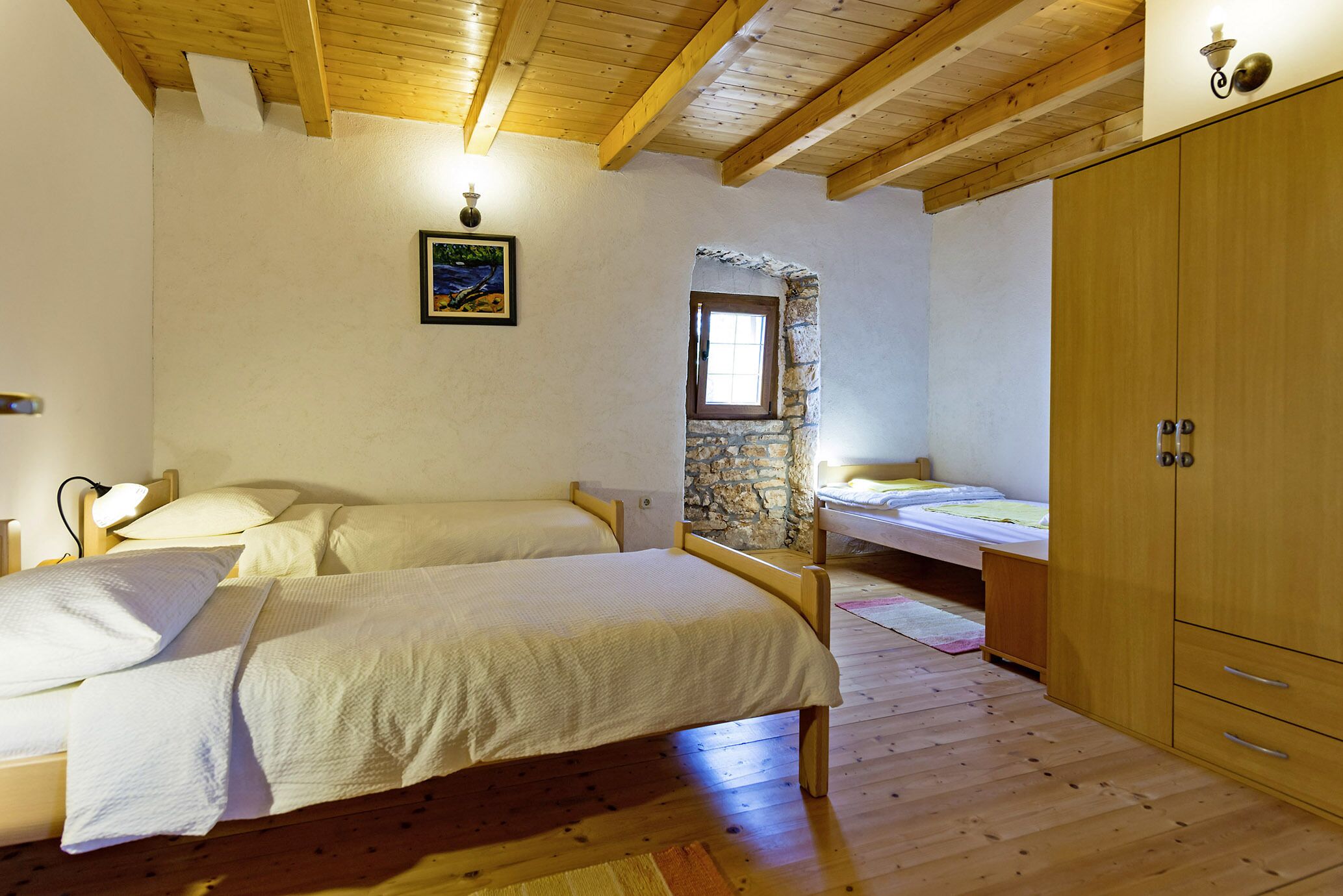 Une chambre avec deux lits, un plancher en bois, un mur en pierre et une armoire en bois.