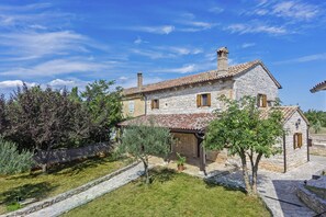A stone house with a tiled roof, a small garden with potted plants, and a stone pathway leading to the entrance.