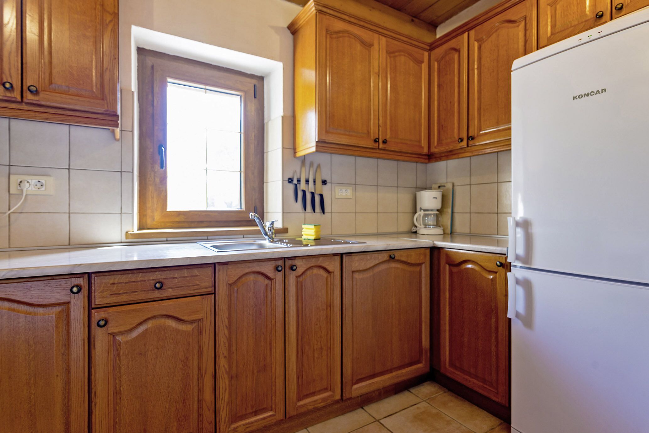 A kitchen with wooden cabinets, a white refrigerator, a window, and a sink.