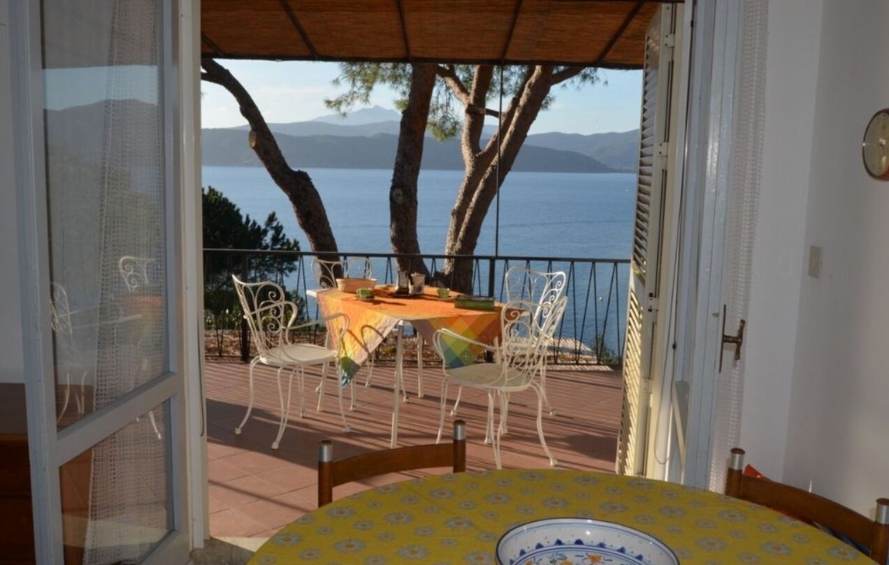 An open balcony with a table set for dining, overlooking a body of water and mountains.