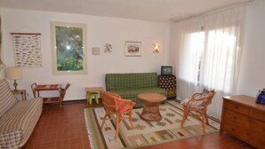 Una sala de estar con un sofá verde, dos sillones de mimbre, una mesita, una lámpara y un cuadro en la pared.