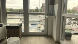 A room with large windows overlooking a marina, wicker furniture, and a white table with a vase. - Maritime boutique vacation apartment AM YACHTHAFEN (Greifswald)