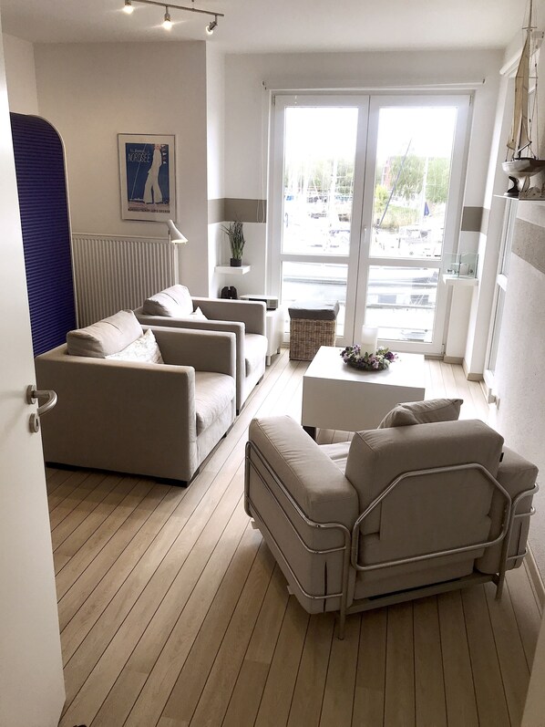 A modern living room with a sofa set, a small table, and a view of the street through large windows.