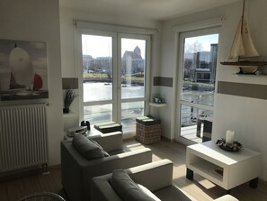 A modern living room with large windows, a sofa, a small table, and a decorative sailboat model.