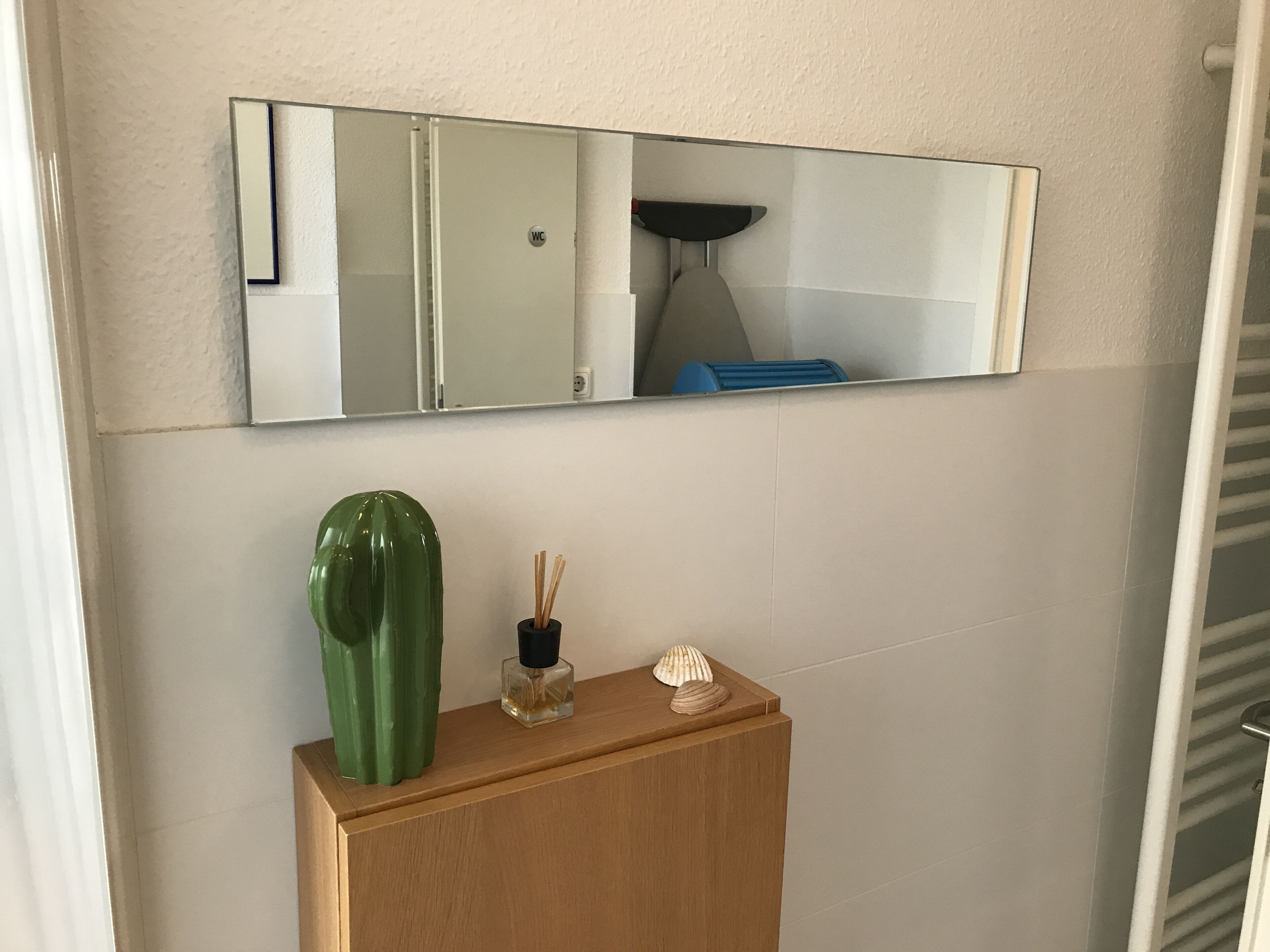 Ein Badezimmer mit einem Holzkosmetikschrank, einem grünen Blumentopf, einer Parfümflasche und einer Muschel.