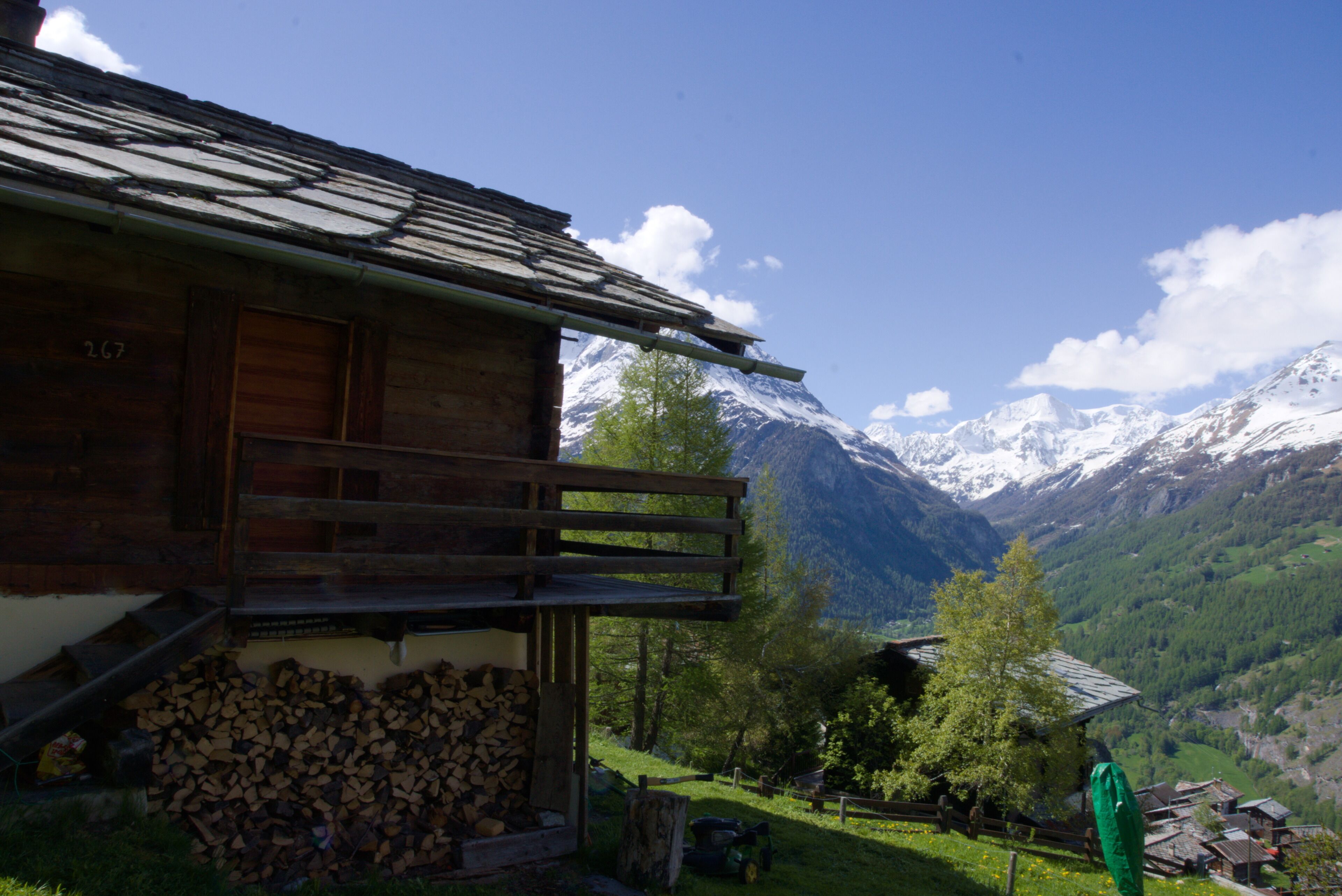 A wooden cabin with a balcony, a pile of firewood, and a mountain backdrop.