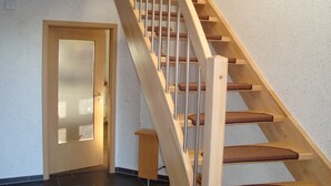 A wooden staircase with a handrail and carpeted steps leading to a door with a frosted glass panel. - Vacation home at the Wangermeer, 3 bedrooms up to 8 pers. charging station / wallbox (Hohenkirchen)