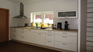 A modern kitchen with white cabinets, a stainless steel range hood, a built-in microwave, and a window with a view of a brick building. - Vacation home at the Wangermeer, 3 bedrooms up to 8 pers. charging station / wallbox (Hohenkirchen)
