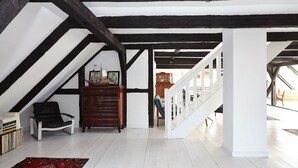 A spacious attic room with exposed wooden beams, a white staircase, and a view of the lower level.