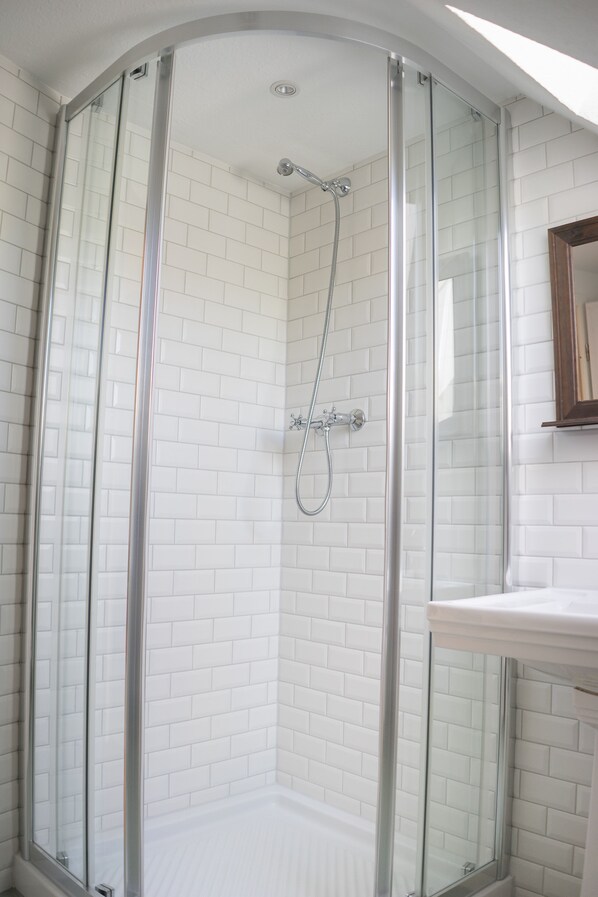 A glass-enclosed shower with white tiled walls and a white sink with a wooden countertop.