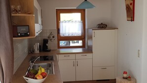 Eine Küche mit einer Holzausziehtheke, einer Fruchtschüssel, einer Kaffeemaschine und einem Fenster mit Vorhang.
