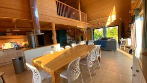 A spacious kitchen with a wooden table and chairs, a balcony, and a view of greenery outside. - Luxury wooden house with garden on the Baltic Sea with sauna / whirlpool near Swinoujscie (Kolczewo)