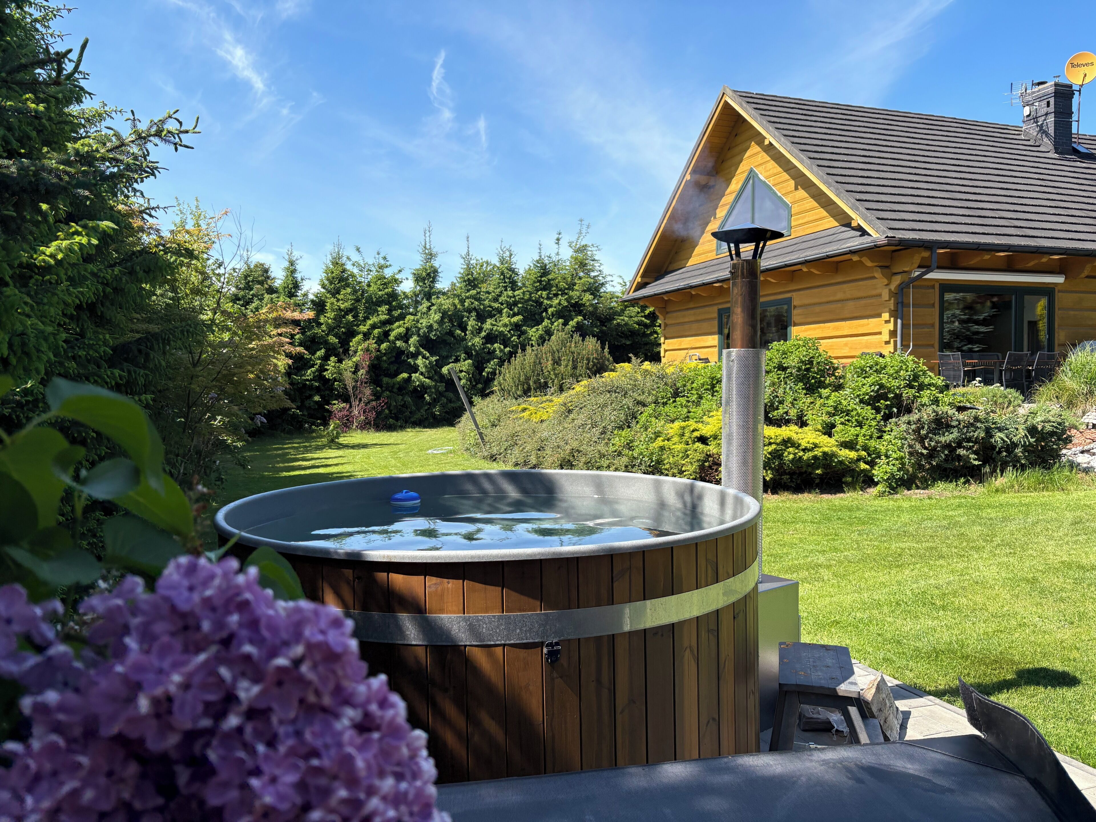 Un bain à remous dans un jardin, avec une maison en bois en arrière-plan.