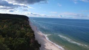 A coastal landscape with a sandy beach, dense forest, and a clear view of the ocean. - Luxury wooden house with garden on the Baltic Sea with sauna / whirlpool near Swinoujscie (Kolczewo)