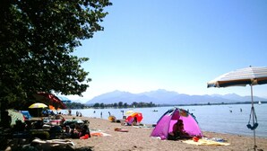 Een strand met tenten en parasols, een zandstrand en boten op het water.