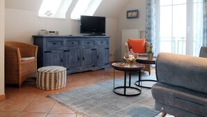 En stue med fjernsyn, sofa, stol, et lille bord med glas og et skab.