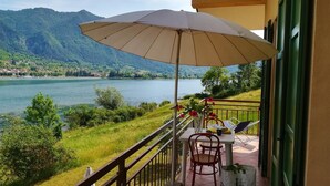 A balcony with a table, chairs, and an umbrella overlooking a lake and mountains. - Directly on the lake on the second floor and with a garden on the first floor (Idro)
