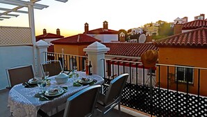 A balcony with a table set for dining, overlooking a residential area with red-tiled roofs and white walls. - Luxury Apartment with Private Garage and Communal Pool. FREE WIFI (Nerja)
