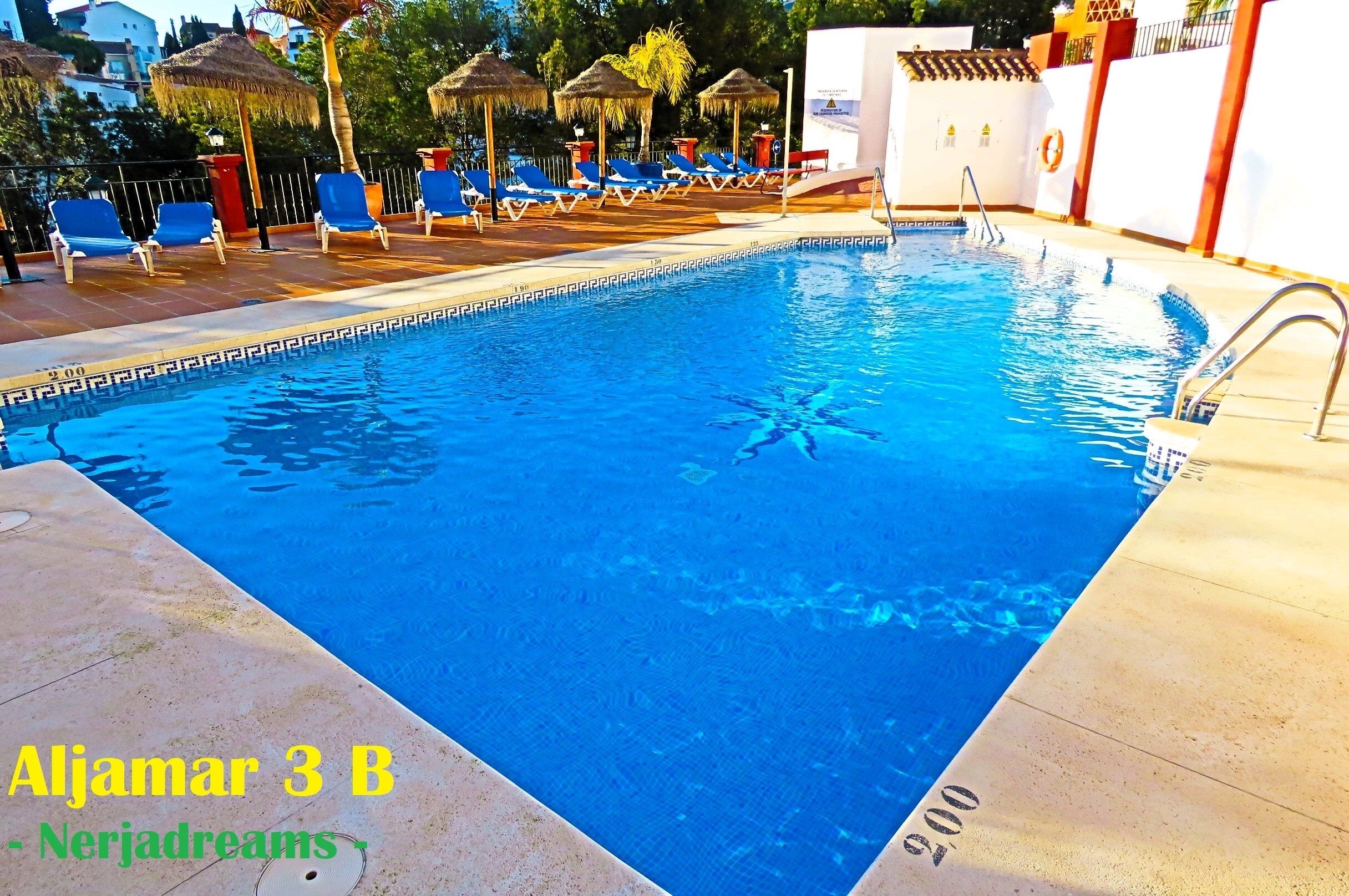 A swimming pool with blue water, surrounded by lounge chairs and umbrellas.