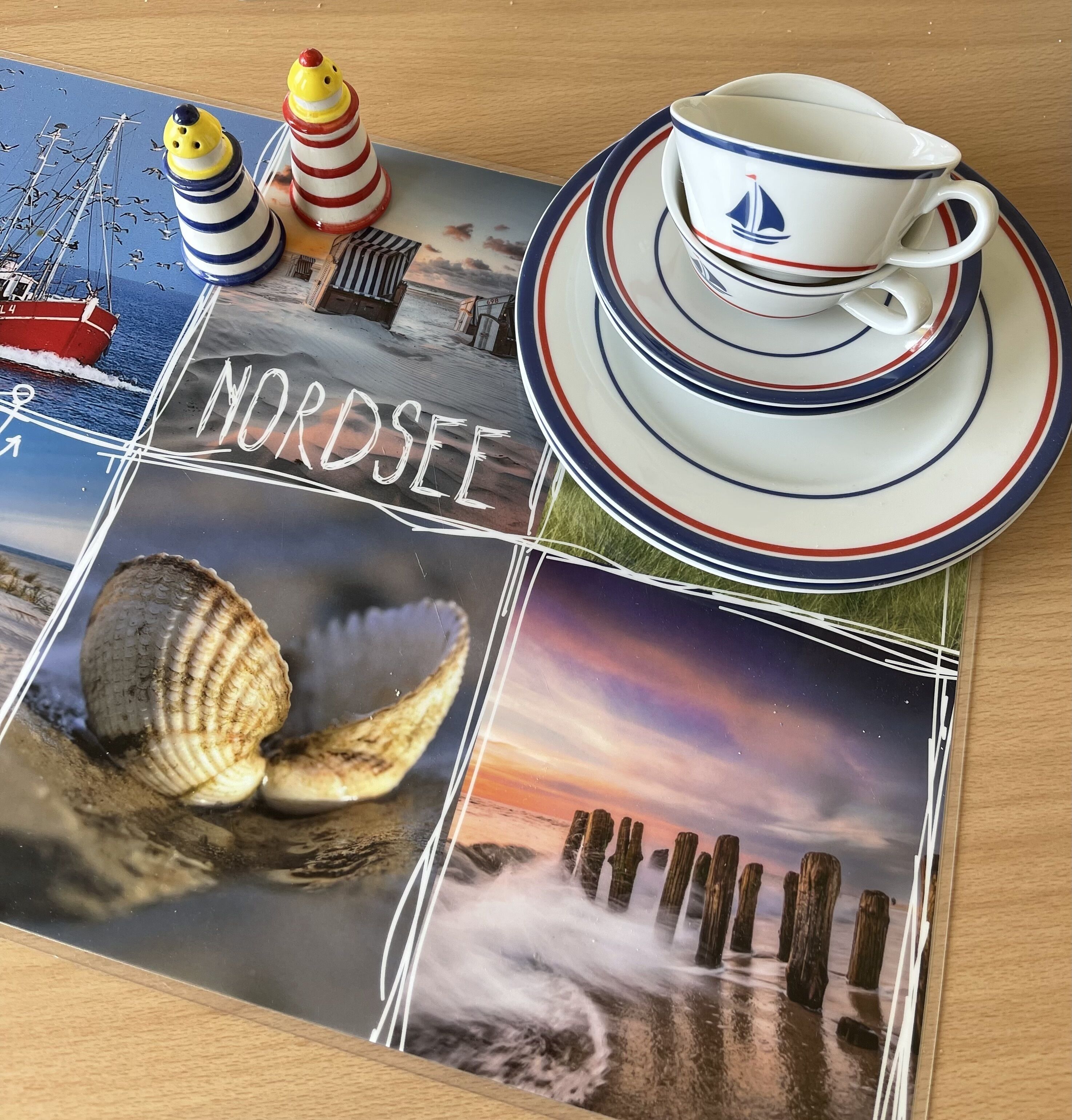 A table with a placemat featuring nautical-themed artwork, a cup and saucer, and two salt and pepper shakers.