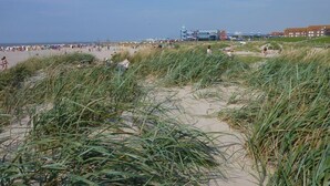 A beach with sand dunes and a building in the background. - Cozy attic studio Norddeich panoramic window with sea view beach 50 meters (Norden)