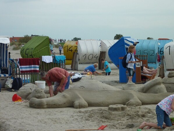 A beach with sand sculptures and numbered beach huts.