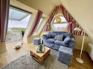 A cozy loft bedroom with a large skylight, a blue sofa, a wooden coffee table, and a fluffy white dog.