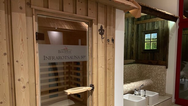 Une porte en bois avec une pancarte indiquant « SAUNA INFRAROUGE 50° » et une vue sur une salle de bain avec une baignoire et un lavabo.