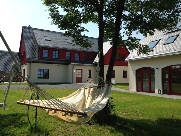 A hammock tied to a tree in a grassy area with a building in the background. - Exclusive ***** 6 apartments for 12-27 persons To Bergwiese (Fürstenau)