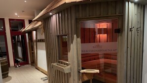 Un sauna aux murs en bois et à la porte en verre, portant l’inscription « Bergwiese Kräuterdampfsau », avec une température de 60 degrés Celsius.