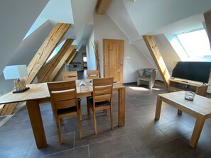 A dining area with wooden furniture and a TV in a loft-style room with sloped ceilings and skylights. - Exclusive ***** 6 apartments for 12-27 persons To Bergwiese (Fürstenau)