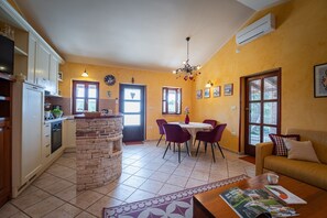 Uma cozinha compacta com uma ilha de pedra, uma área de refeições com cadeiras roxas, um sofá e uma mesa de centro com uma revista.