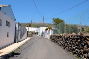 A narrow street with white buildings, a stone wall, and a clear blue sky.