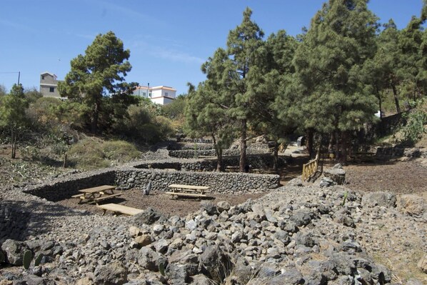A rocky outdoor area with stone walls, picnic tables, and trees.