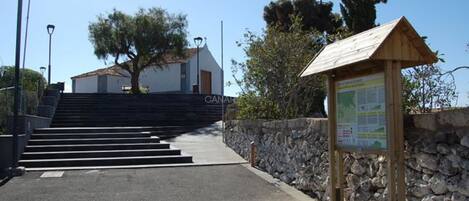 Un mur de pierre, une enseigne en bois et, au fond, un bâtiment sur lequel on peut lire le mot « CANAL ».