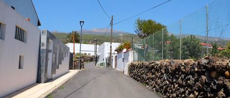 A narrow street with white buildings, a stone wall, and a clear blue sky.