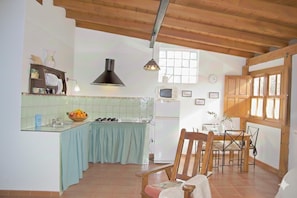 A kitchen with a dining area, wooden ceiling beams, a refrigerator, and a window.
