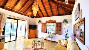 A spacious living room with a wooden ceiling, a sliding glass door leading to a balcony, a television, and a sofa. - Großzüg. House with panoramic views of sea, mountains & valley + optional apartment (Tajuya)